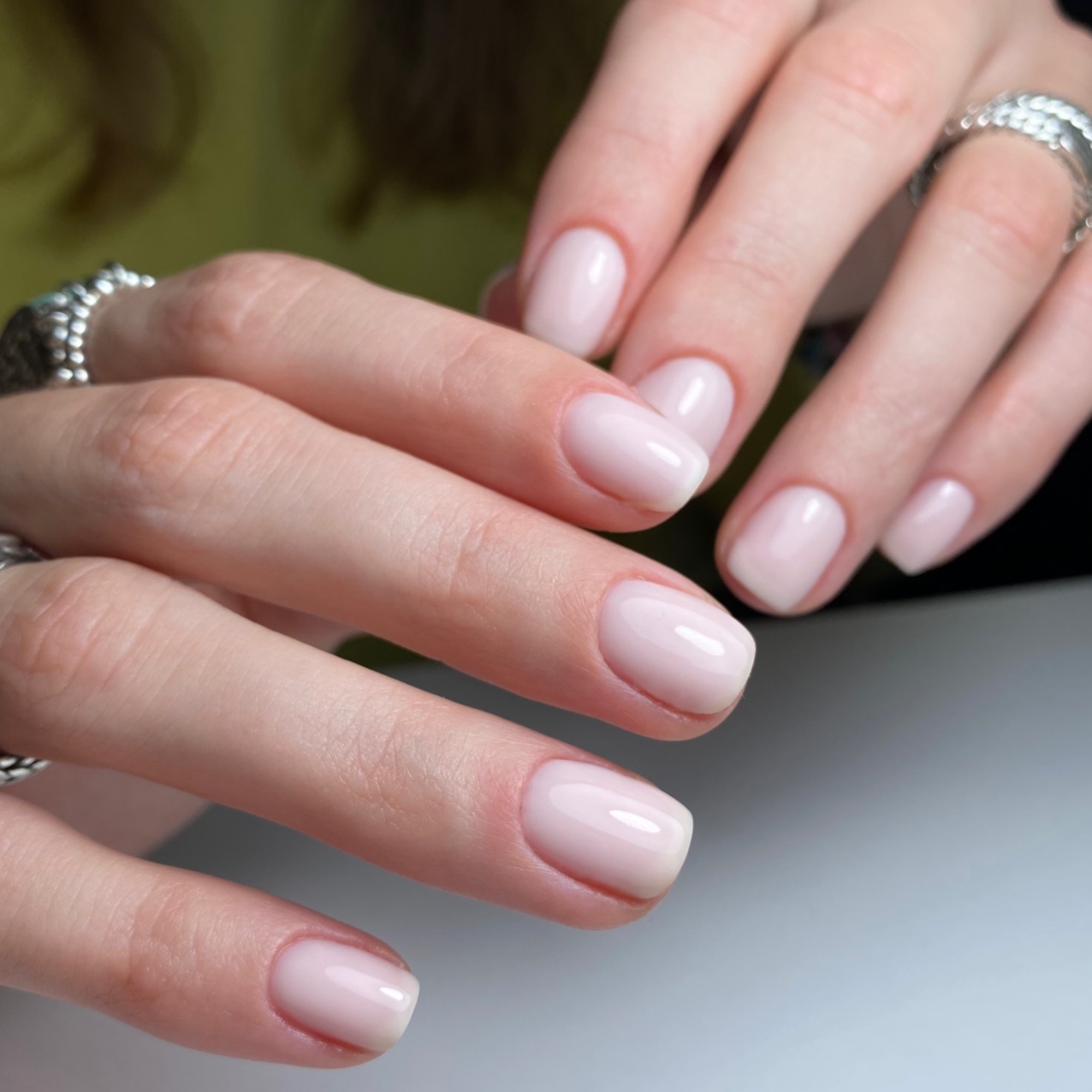 Melkwitte BIAB-nagels op twee handen met zilveren ringen