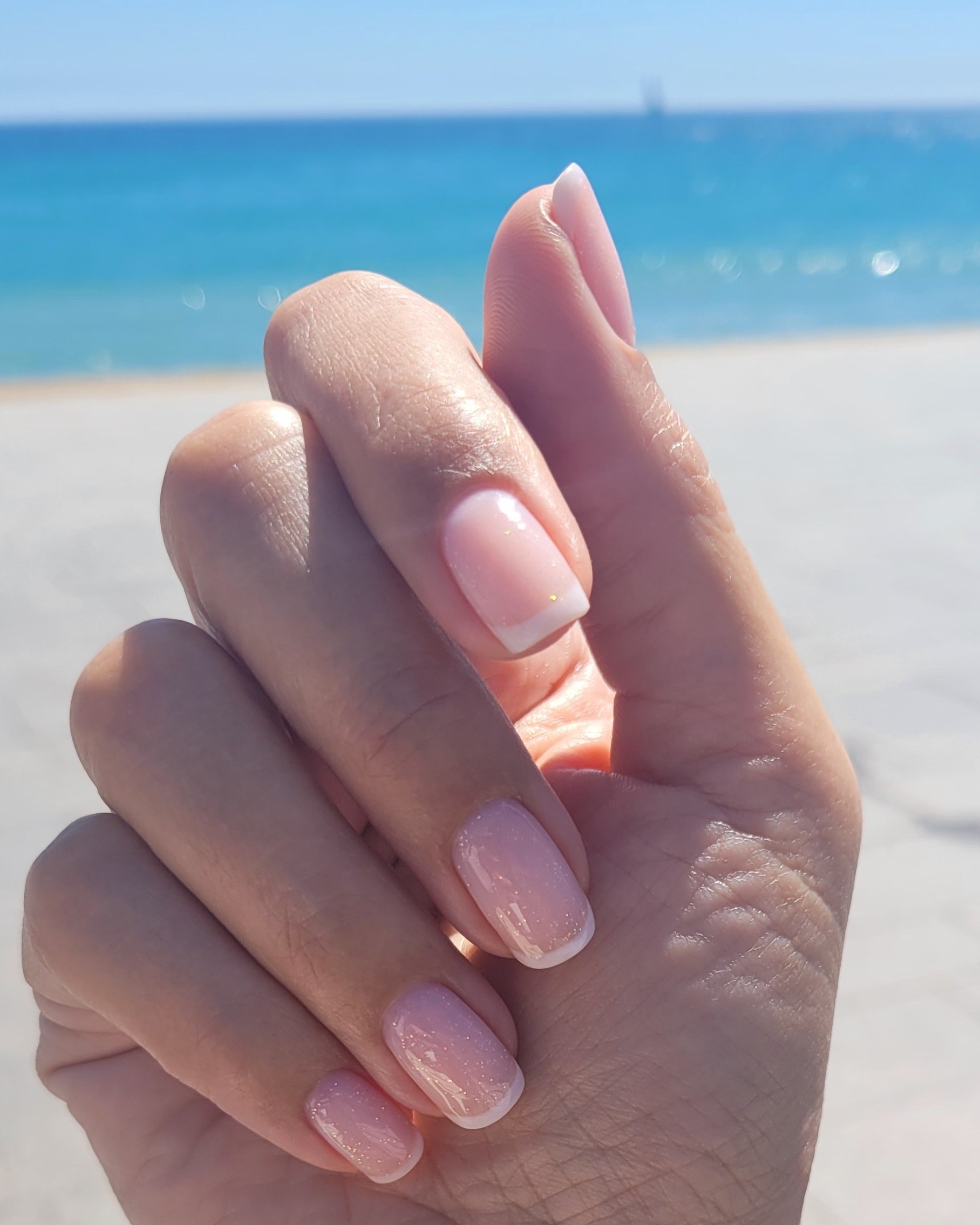 Roze nagels met witte randjes, hand omhoog aan zee