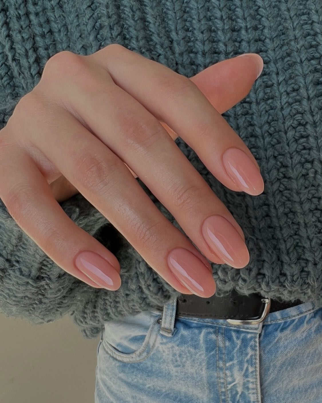 Nude amandelvormige nagels tegen een grijze gebreide trui
