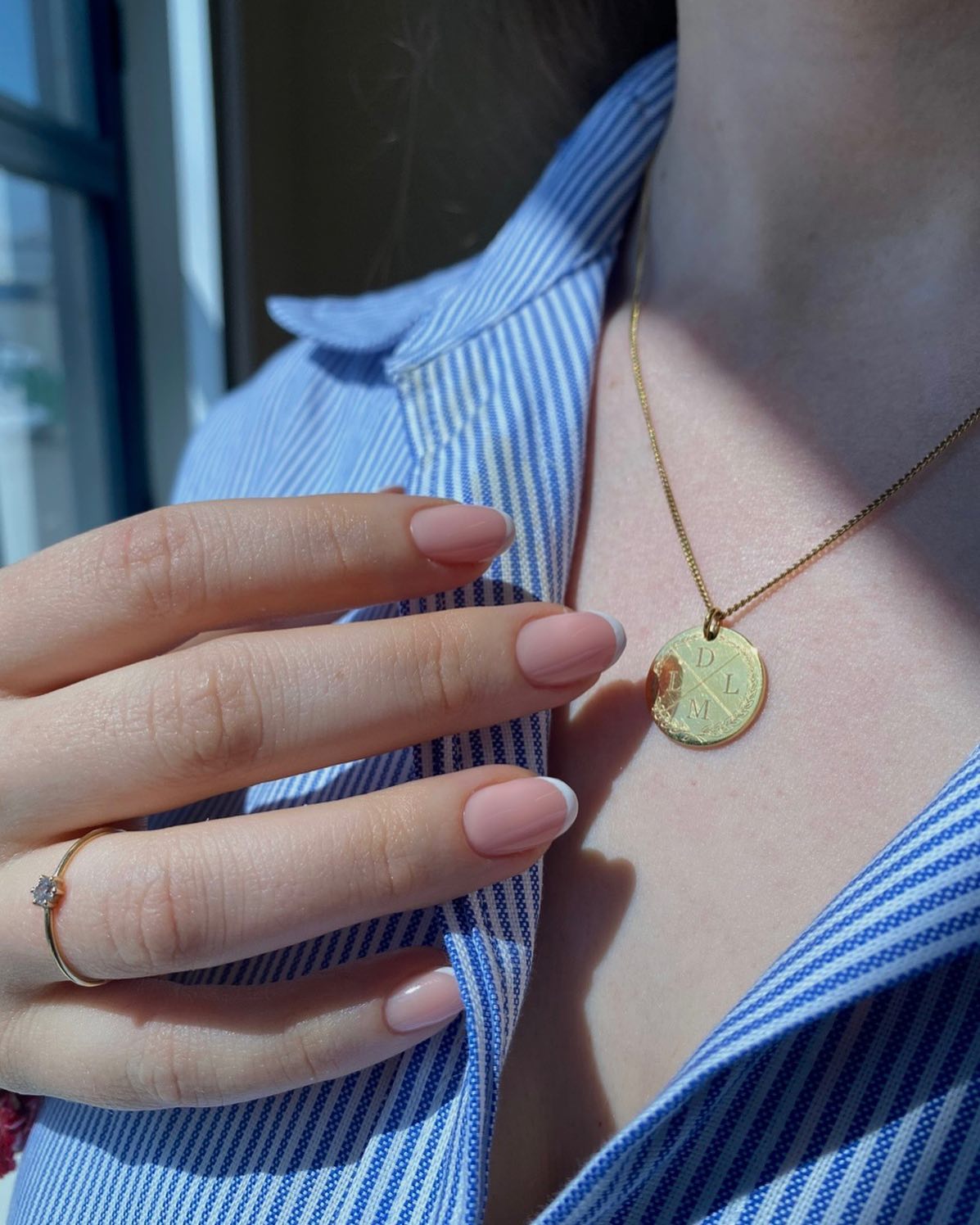 Roze nagels tegen een blauw gestreepte blouse met gouden ketting