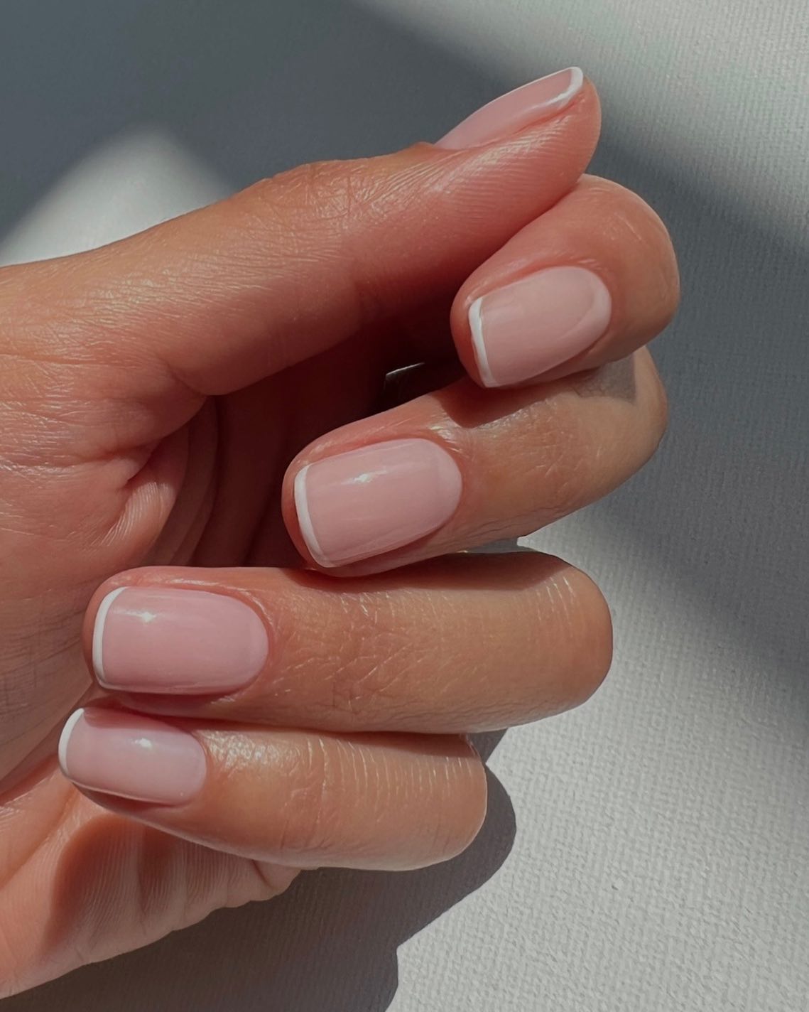 Korte nagels met een zachte witte french in het licht van het raam